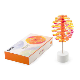 Lollipopter Mango Solid is a colorful toy featuring a vibrant orange and pink design. It consists of a series of layered discs resembling a blooming flower on a sturdy white base. The product is displayed next to its stylish packaging that features soft pastel colors and the Lollipopter logo.