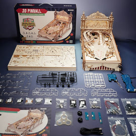 A detailed display of the Robotime 3D Pinball DIY kit, featuring an unassembled wooden pinball machine along with various components such as boards, mechanical parts, and tools. The kit is designed for building a classic pinball game with intricate details and multiple shooting score challenges. The packaging is showcased alongside the pieces, hinting at an engaging hands-on crafting experience.