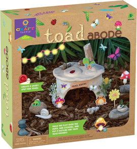 The Toad Abode DIY kit by PlayMonster, featuring a cozy, clay toad shelter with decorative elements like mushrooms, colorful insects, and a 'Toad Crossing' sign. The box displays engaging instructions to mold clay and add stickers for a whimsical outdoor habitat for toads.