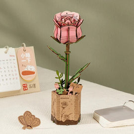 The Pink Rose Model by Robotime is a beautifully crafted DIY kit featuring a detailed pink rose flower atop a green stem, set in a rustic wooden pot. The pot is adorned with small flowers and a tag that says 'for you', providing an elegant touch. Ideal for decoration or as a heartfelt gift, this model combines artistry with a hands-on crafting experience.