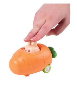 A child’s hand presses down on the Press and Go Carrot Car, a bright orange toy resembling a carrot with a bunny peeking out. The toy features two green wheels and a vibrant design, ideal for engaging kids in imaginative play and developing hand-eye coordination.