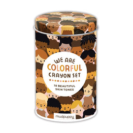 We Are Colorful Crayon Set by Mudpuppy features a cylindrical container adorned with diverse illustrated faces. Inside are 18 crayons in various skin tones, perfect for expressive and inclusive creativity.