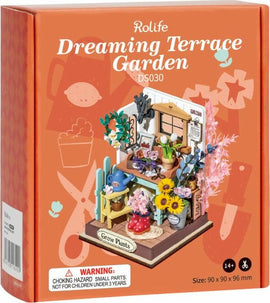 The DIY Dreaming Terrace Garden kit by Robotime showcases a charming miniature scene, featuring a colorful arrangement of potted flowers, a wooden table, and gardening tools. The vibrant design includes sunflowers, a watering can, and an array of plants, perfect for DIY enthusiasts who enjoy crafting detailed environments. The box highlights the kit's dimensions and a warning for small parts, ideal for ages 14 and up.