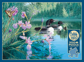 Iris Cove Loons jigsaw puzzle by Cobble Hill featuring a serene lakeside scene with two loons swimming in crystal-clear water surrounded by vibrant flowers and a butterfly. The artwork captures the tranquility of nature, making this a perfect 500-piece puzzle for nature lovers and puzzle enthusiasts alike.