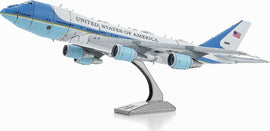 A detailed metal model of Air Force One, showcasing its iconic blue and white color scheme, with the words 'United States of America' on the fuselage. The model is displayed on a sturdy base, highlighting the aircraft's sleek design and three prominent engines.