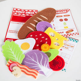 Colorful felt pieces representing various sandwich ingredients, including lettuce, tomato, cheese, bacon, and a fried egg, accompanied by a guest check order pad and a matching game card. The vibrant elements encourage creative play and learning about food.