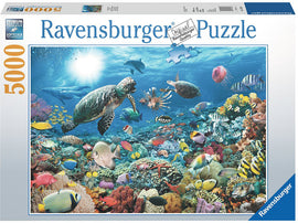 Beneath the Sea 5000 piece jigsaw puzzle by Ravensburger featuring a vibrant underwater scene. The image showcases colorful fish, corals, a sea turtle, and other marine life under a bright blue ocean with sunlight filtering through the water.