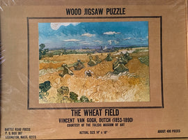A wood jigsaw puzzle featuring 'The Wheat Field' by Vincent Van Gogh. The box showcases a vibrant landscape painting of golden wheat fields with dynamic sky and figures. It is produced by Battle Road Press and contains about 400 pieces, with dimensions 14" x 18".
