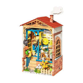 The Dream Yard Model Kit by Robotime showcases a charming miniature cottage with detailed features, including a welcoming front door, colorful potted plants, and a classic red-tiled roof. The intricate design captures a cozy outdoor setting, perfect for DIY enthusiasts.