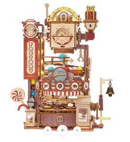 A detailed Chocolate Factory Marble Run Model Kit by Robotime, featuring intricate wooden components, colorful balls rolling through a mechanical system, candy-themed decorations, and a small bell. This DIY kit presents a whimsical and playful design, ideal for creativity and hands-on fun.
