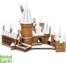 A detailed metal model of Hogwarts Castle covered in snow, featuring intricate towers, spires, and architectural details. The castle is depicted in a warm bronze color against a white background, showcasing its enchanting winter charm.