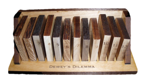 Dewey's Dilemma is a mechanical puzzle featuring a wooden base with numbered blocks arranged in a row. Each block is crafted from different types of wood, showcasing a rich color variation. The puzzle challenges users to arrange the blocks in a specific order, enhancing problem-solving skills and providing a tactile experience. The wooden base is engraved with the product name, adding a touch of elegance to this captivating brain teaser.