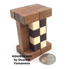 An intricately designed hourglass wooden mechanical puzzle by Pelikin Puzzles. The puzzle features interlocking wooden pieces in various shades, resembling an hourglass shape, with a coin placed beside it for size comparison. Perfect for puzzle enthusiasts who appreciate craftsmanship and complexity.