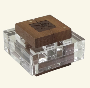 The Glitter Burr is a captivating mechanical puzzle made from a combination of wood and acrylic materials. The puzzle features a square wooden top with a logo and four wooden pieces, enclosed within a transparent acrylic base. Its intricate design and unique construction invite challenging and engaging play, making it a delightful addition to any puzzle enthusiast's collection.