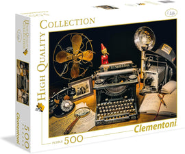 The Typewriter jigsaw puzzle by Clementoni, featuring a nostalgic scene with an antique typewriter, vintage camera, classic telephone, and old photographs. The box showcases high-quality graphics that highlight the puzzle's design, making it appealing to puzzle enthusiasts and collectors alike.