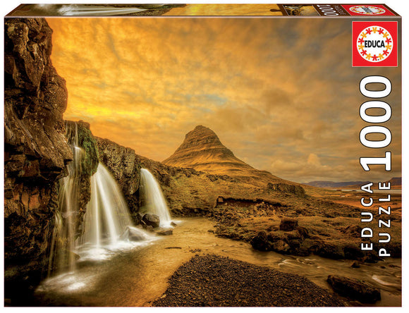 The KIRKJUFELLSFOSS WATERFALL jigsaw puzzle box by Educa showcases a stunning scenic view of Kirkjufell mountain with cascading waterfalls, set against a vibrant sunset sky. The box features 1000 pieces and displays an enchanting landscape, ideal for puzzle enthusiasts and nature lovers alike.