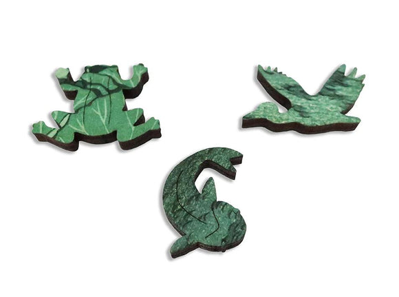A close-up of three unique jigsaw puzzle pieces from the Shiba Benten Pond design by Artifact Wooden Puzzles. The pieces feature intricate green motifs resembling a frog, a bird, and a pond creature, showcasing the artistic detailing and craftsmanship of the wooden puzzle.