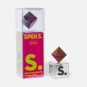 The Speks Stripes Jazzy product is showcased in a vibrant, clear packaging. Inside, a colorful magnetic cube made of small spheres is displayed. The packaging features bright pink and green colors with playful typography, highlighting its 'spectacularly magnetic' feature.