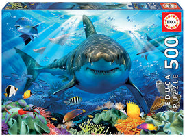 Educa 500-piece jigsaw puzzle featuring a majestic great white shark swimming in a vibrant underwater scene filled with colorful fish and coral reefs. The captivating artwork showcases a diverse marine ecosystem, perfect for puzzle enthusiasts and ocean lovers.