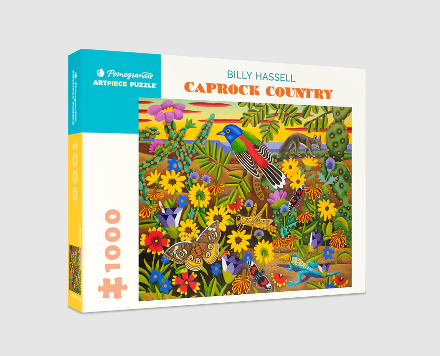 Caprock Country jigsaw puzzle by Billy Hassell featuring a vibrant landscape filled with colorful flowers, butterflies, cacti, and wildlife, packaged in a stylish box. The illustration showcases bright colors and intricate details characteristic of Hassell's artwork.