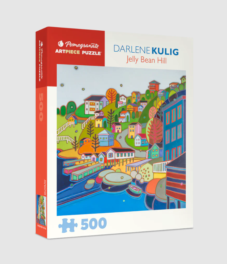 The Jellybean Hill jigsaw puzzle by Pomegranate features a vibrant and colorful illustration by Darlene Kulig, depicting a whimsical village scene with charming houses, rolling hills, and scenic waterways. The puzzle contains 500 pieces and is packaged in a decorative box, showcasing the artwork on the front.