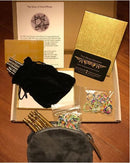 The Nova Plexus Limited Edition Pair, a mechanical puzzle by Two Brass Monkeys, displayed in a box. Inside are golden packaging, a story card, a velvet pouch containing brass and steel pieces, and colorful rubber bands.