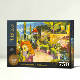 Art & Fable Puzzle Co jigsaw puzzle titled 'Lake Como Breeze'. Features a vibrant, artistic depiction of a serene lakeside scene with colorful architecture and lush greenery. Box contains 750 pieces and highlights a velvet-touch surface for a superior feel. Includes a high-quality print inside.