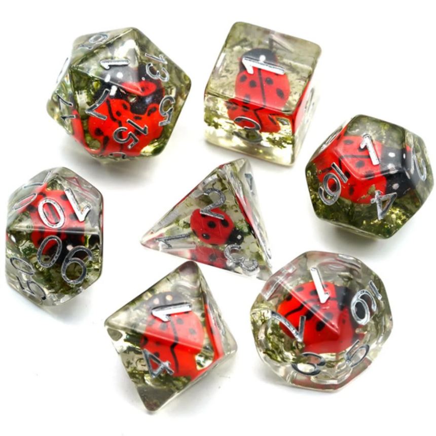 A set of seven red ladybug-themed RPG dice by Foam Brain Games, featuring transparent resin bodies with embedded ladybug designs and illuminated numbering. The set includes various shapes, such as a d20, d12, d10, d8, d6, and d4, perfect for tabletop gaming enthusiasts.