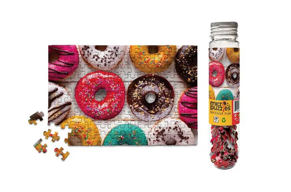 A colorful 150-piece jigsaw puzzle featuring a variety of donuts, including frosted and sprinkled options. The puzzle is partially completed, displaying the vibrant designs of the donuts. Beside the puzzle, there is a clear glass bottle with a colorful label that showcases the same donut design, enhancing its appeal as a fun and engaging puzzle option.