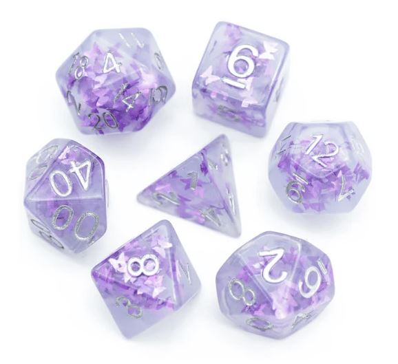 A collection of Lavender Butterfly RPG dice set by Foam Brain. The set includes seven polyhedral dice, featuring a translucent lavender color with delicate purple flakes and silver numbers. Each die varies in shape, including a d20, d12, d10, d8, d6, and d4, making it perfect for tabletop role-playing games.