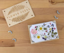 A wooden flower press set from Gift Republic, featuring a beautifully engraved 'FLOWER PRESS' label. The kit includes a wooden frame, pressed flowers, and securing screws displayed on a wooden surface, ideal for DIY floral crafts.