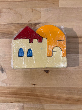 A colorful wooden jigsaw puzzle featuring a stylized house with a red roof, blue windows, and a large orange sun. The pieces are made from natural wood and are intricately shaped, showcasing vibrant colors. Wrapped in clear plastic, the puzzle emphasizes creativity and tactile play for children.