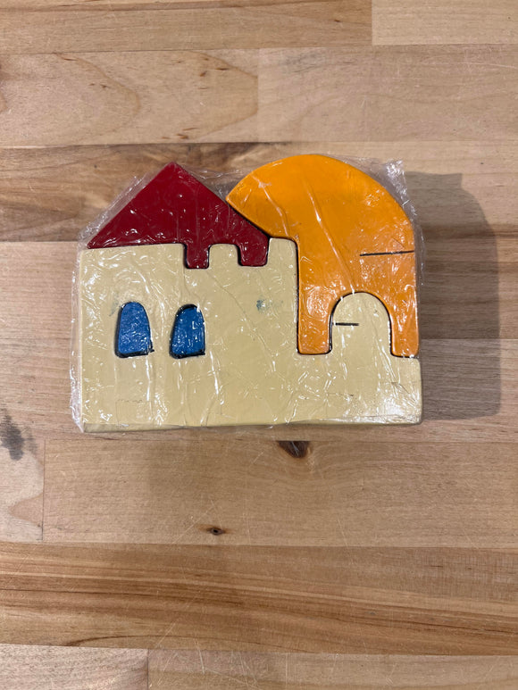 A colorful wooden jigsaw puzzle featuring a stylized house with a red roof, blue windows, and a large orange sun. The pieces are made from natural wood and are intricately shaped, showcasing vibrant colors. Wrapped in clear plastic, the puzzle emphasizes creativity and tactile play for children.