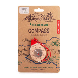 Huckleberry Compass by Kikkerland Design Inc. A red and wooden compass featuring directional indicators. The packaging includes illustrations of mountains and trees, highlighting its outdoor theme.