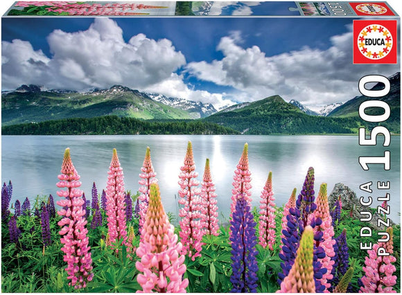 A beautiful 1500-piece jigsaw puzzle by Educa featuring vibrant lupins in shades of pink and purple, set against a serene lakeside scene with mountains in the background and fluffy clouds in the sky.