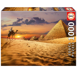 CAMEL IN THE DESERT 1000PC jigsaw puzzle by Educa featuring a beautifully illustrated scene of a camel and rider in a sandy desert landscape with pyramids in the background during sunset.