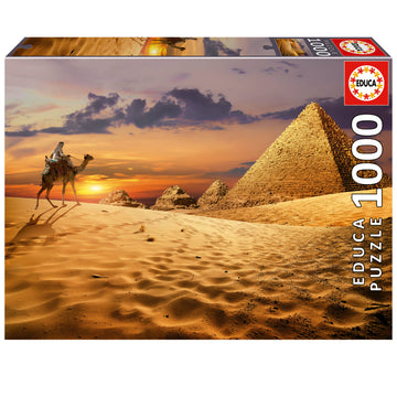 CAMEL IN THE DESERT 1000PC jigsaw puzzle by Educa featuring a beautifully illustrated scene of a camel and rider in a sandy desert landscape with pyramids in the background during sunset.