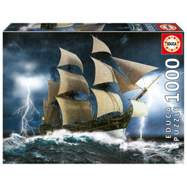 Educa's 'PERFECT STORM' jigsaw puzzle featuring a dramatic scene of a majestic ship battling through a stormy sea with waves crashing and lightning illuminating the dark sky. The puzzle consists of 1000 pieces, showcasing intricate details of the ship's sails and turbulent waters, providing an engaging and challenging experience for puzzle enthusiasts.