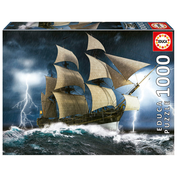 Educa's 'PERFECT STORM' jigsaw puzzle featuring a dramatic scene of a majestic ship battling through a stormy sea with waves crashing and lightning illuminating the dark sky. The puzzle consists of 1000 pieces, showcasing intricate details of the ship's sails and turbulent waters, providing an engaging and challenging experience for puzzle enthusiasts.