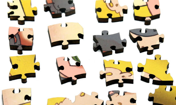 A close-up view of jigsaw puzzle pieces from the Tea Bath puzzle by Stasia Burrington. The pieces showcase colorful illustrations with shades of yellow, pink, and gray, featuring playful and whimsical designs that invite creativity. Each piece is crafted from wood, emphasizing quality and durability.