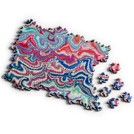 A vibrant jigsaw puzzle titled 'Small Marbling Infinity Blue' by Nervous System. The puzzle features an intricate marbled design with swirling patterns in shades of blue, red, and pink. Several scattered pieces surround the main puzzle, showcasing the unique colors and shapes that make this puzzle visually striking and engaging.