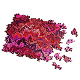 A vibrant jigsaw puzzle titled 'Small Marbling Infinity Red' by Nervous System. The puzzle features swirling patterns in shades of red, pink, and purple, showcasing intricate designs with unique pieces scattered around it, highlighting the artistic and engaging nature of the product.