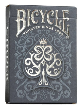 Bicycle Cinder card game box featuring an ornate dark gray design with intricate patterns. The prominent spade symbol is elegantly adorned, and the text 'Bicycle' is displayed at the top. The box showcases high-quality craftsmanship characteristic of US Playing Card Co.