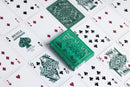 A close-up view of a Bicycle Jacquard playing card deck, featuring intricate green designs and classic playing cards displayed in a random layout. The deck is positioned prominently with several face and number cards visible, showcasing the distinct art style of the US Playing Card Company.