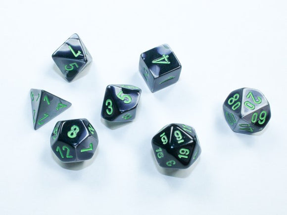 A set of Mini Gemini RPG dice in black and grey with bright green numbers. The set includes seven polyhedral dice, each displaying different shapes and numbers, ideal for tabletop gaming enthusiasts.