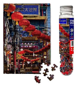 Micro Puzzle featuring a vibrant image of Chinese lanterns hanging in a bustling street market. The puzzle includes several interlocking pieces beside a clear storage tube, showcasing colorful pieces and a detailed visual of the scene.