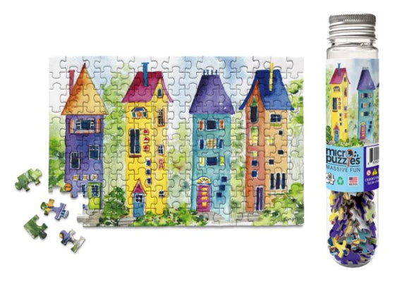 A colorful jigsaw puzzle featuring whimsical gnome houses in vibrant colors, including reds, blues, yellows, and greens. The completed puzzle is shown alongside a clear container holding spare pieces, emphasizing its charming design.