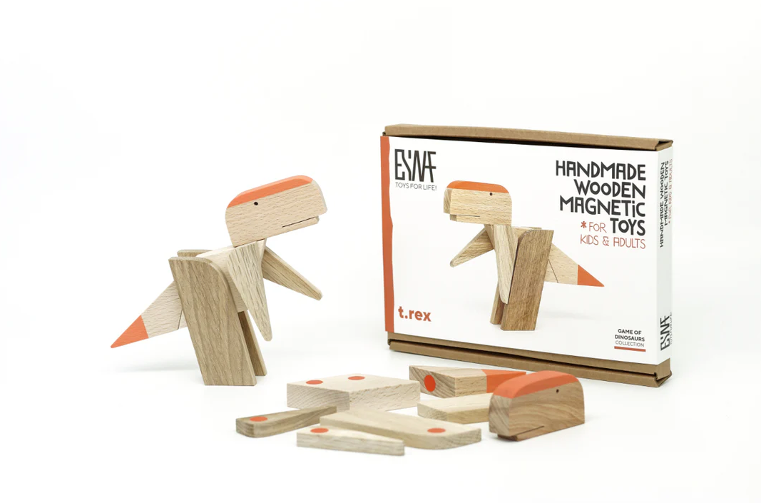 Handmade wooden T. Rex magnet from Esnf Toys, featuring a cute, simplistic dinosaur design made from natural wood with orange accents. The package shows the toy alongside several wooden pieces to assemble or create variations.