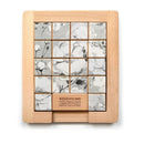 A wooden mechanical sliding puzzle featuring black and white floral designs. The puzzle consists of a grid of tiles that can be rearranged to complete the image. The base has a wood finish with an instruction label that says 'REMOVE ME' for interaction, highlighting its playful nature. The background is minimalist to emphasize the puzzle's intricate details.