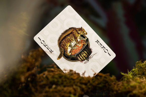 A close-up of an 'Extinct Animals' playing card featuring a detailed illustration of a leopard sitting on a mushroom. The card displays the word 'JOKER' prominently, surrounded by decorative elements. The background showcases a natural setting with blurred greenery, enhancing the card's artistic design.